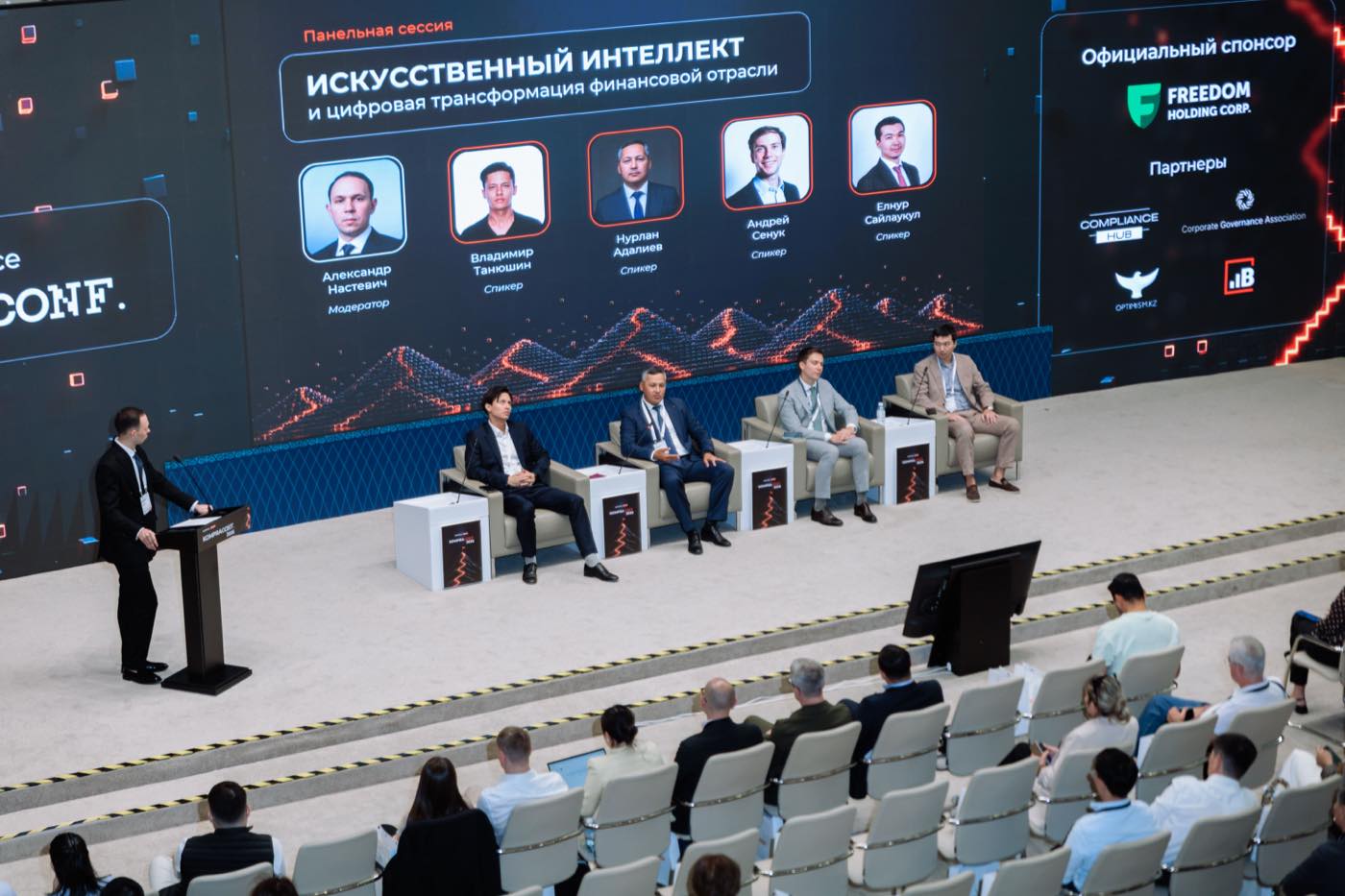 Панельная сессия на KompraConf 2026: модератор у трибуны и четыре спикера на сцене